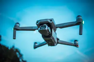 Ilustrasi: Sebuah drone modern berwarna abu-abu sedang terbang di langit biru.