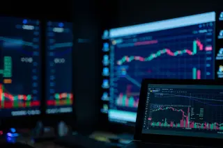 Ilustrasi: Layar monitor dan laptop menampilkan grafik pergerakan harga saham di ruangan gelap.