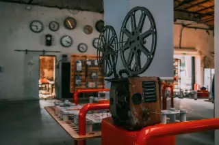 Ilustrasi: Proyektor film antik dipajang di dalam ruangan berkonsep industrial dengan hiasan jam dinding.