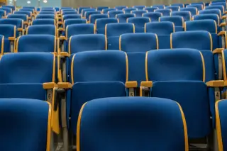 Ilustrasi: Deretan kursi auditorium berwarna biru yang kosong menghadap ke depan.