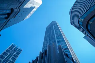 Ilustrasi: Sudut pandang rendah deretan gedung pencakar langit modern berlatar belakang langit biru.