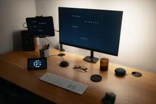 Ilustrasi: Meja kerja kayu dengan monitor komputer, papan ketik, tetikus, dan gawai modern.
