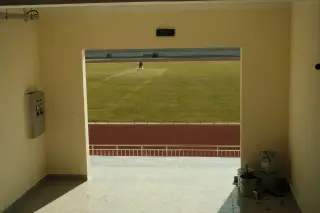 Ilustrasi: Pemandangan dari dalam lorong bangunan ke arah lapangan rumput dan lintasan lari stadion.