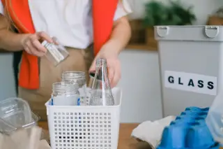 Ilustrasi: Seseorang memilah botol dan toples kaca di dekat wadah daur ulang.