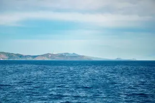 Ilustrasi: Pemandangan laut lepas berwarna biru dengan pulau perbukitan di kejauhan di bawah langit cerah.