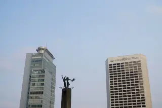 Ilustrasi: Patung Selamat Datang diapit gedung-gedung bertingkat dengan latar belakang langit cerah.