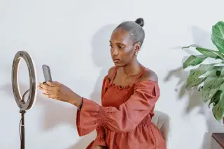 Ilustrasi: Seorang wanita mengatur ponsel pada tripod ring light di dalam ruangan.