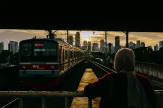 Ilustrasi: Kereta commuter line melintas berlatar gedung-gedung bertingkat Jakarta saat senja.