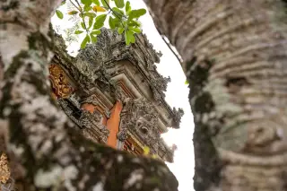 Ilustrasi: Detail ukiran atap bangunan tradisional Bali di antara batang pohon.