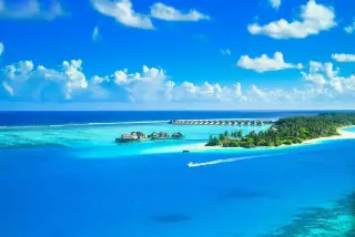 Ilustrasi: Pemandangan udara pulau tropis dengan resor tepi pantai dan perairan biru jernih.