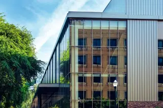 Ilustrasi: Sudut bangunan modern berdinding kaca yang memantulkan gedung bata di sebelahnya.