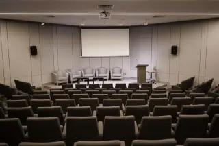 Ilustrasi: Deretan kursi di dalam auditorium kosong yang menghadap ke panggung kecil.
