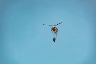 Ilustrasi: Sebuah helikopter pemadam membawa kantong air terbang di bawah langit biru.