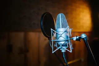 Ilustrasi: Mikrofon studio profesional dengan filter pop terpasang pada penyangga di ruang rekaman.