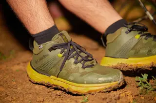 Ilustrasi: Sepasang kaki mengenakan sepatu lari atau trekking berwarna hijau di atas tanah berlumpur.