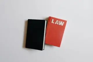 Ilustrasi: Buku merah bertuliskan LAW dan buku hitam di atas latar putih.