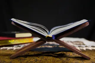 Ilustrasi: Sebuah kitab terbuka di atas rehal kayu dengan latar belakang gelap.