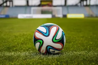 Ilustrasi: Sebuah bola sepak bermotif warna-warni tergeletak di rumput lapangan dengan latar gawang.