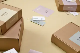 Ilustrasi: Kotak-kotak kardus kemasan pengiriman produk beserta kartu label di atas meja.