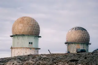 Ilustrasi: Dua kubah radom radar di atas bukit berbatu dengan latar langit berawan.