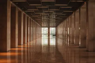 Ilustrasi: Lorong gedung berdinding marmer dengan deretan pilar simetris dan lantai berkilau.