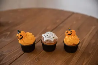 Ilustrasi: Tiga kue mangkuk berhias labu dan jaring laba-laba bertema Halloween di atas meja kayu.