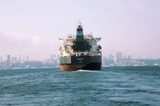 Ilustrasi: Sebuah kapal tanker berlayar di perairan dengan latar belakang pemandangan kota di kejauhan.