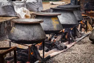 Ilustrasi: Deretan panci logam besar di atas tungku kayu bakar di luar ruangan.