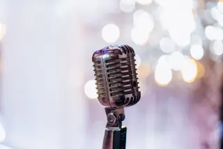 Ilustrasi: Mikrofon bergaya vintage berbahan logam dengan latar belakang lampu bokeh.