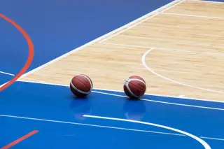 Ilustrasi: Dua bola basket tergeletak di atas lantai lapangan basket dalam ruangan berwarna biru dan kayu.