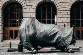 Ilustrasi: Patung banteng tertutup terpal abu-abu di depan gedung dengan jendela melengkung.