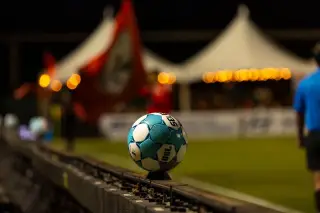 Ilustrasi: Sebuah bola sepak diletakkan di pinggir lapangan pada malam hari dengan latar belakang stadion yang buram.