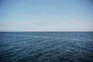 Ilustrasi: Hamparan laut biru berombak tenang di bawah langit biru yang cerah.