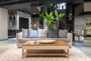 Ilustrasi: Sofa dengan bantal dan meja kayu di dalam ruang pamer furnitur modern.