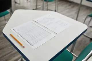 Ilustrasi: Lembar ujian dan pensil tergeletak di atas meja kelas yang kosong.