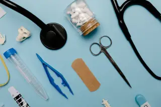 Ilustrasi: Tata letak datar stetoskop, gunting medis, obat-obatan, dan alat kesehatan lainnya di atas meja biru.