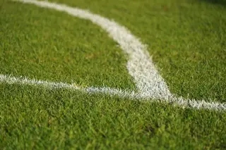 Ilustrasi: Garis putih melengkung di atas rumput hijau lapangan sepak bola.