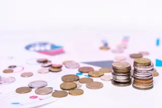 Ilustrasi: Tumpukan dan sebaran koin logam di atas kertas dokumen finansial berlatar putih.