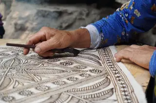 Ilustrasi: Tangan seorang perajin sedang menggambar pola tradisional pada kain menggunakan alat lilin.