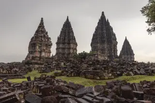 Ilustrasi: Kompleks Candi Prambanan dengan latar belakang langit mendung dan bebatuan di bagian depan.
