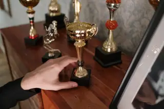 Ilustrasi: Tangan seseorang meraih piala logam emas di atas lemari kayu.