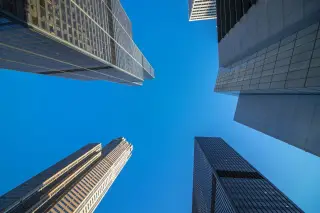 Ilustrasi: Sudut pandang rendah beberapa gedung pencakar langit dengan latar belakang langit biru cerah.