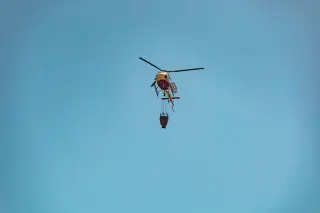 Ilustrasi: Sebuah helikopter pemadam membawa kantong air terbang dengan latar belakang langit biru.