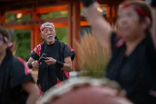 Ilustrasi: Seorang pria lansia mengenakan pakaian tradisional Jepang memegang stik taiko dalam sebuah pertunjukan.