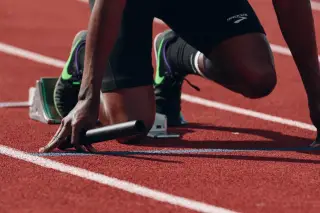 Ilustrasi: Pelari bersiap di garis start lintasan atletik sambil memegang tongkat estafet.