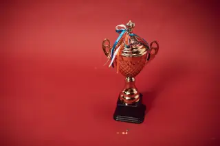 Ilustrasi: Sebuah piala berwarna emas dengan pita warna-warni berlatar belakang merah polos.