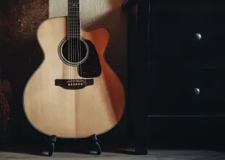 Ilustrasi: Sebuah gitar akustik bersandar pada penyangga di samping laci kayu hitam.