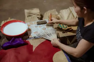 Ilustrasi: Seorang perajin sedang merakit kipas tangan tradisional berbahan bambu dan kain.