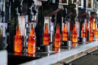 Ilustrasi: Deretan botol kaca berpendar di jalur mesin produksi otomatis di dalam pabrik.