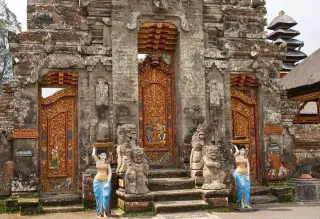 Ilustrasi: Gerbang pura tradisional khas Bali dengan pintu kayu berukir dan beberapa patung penjaga di depannya.